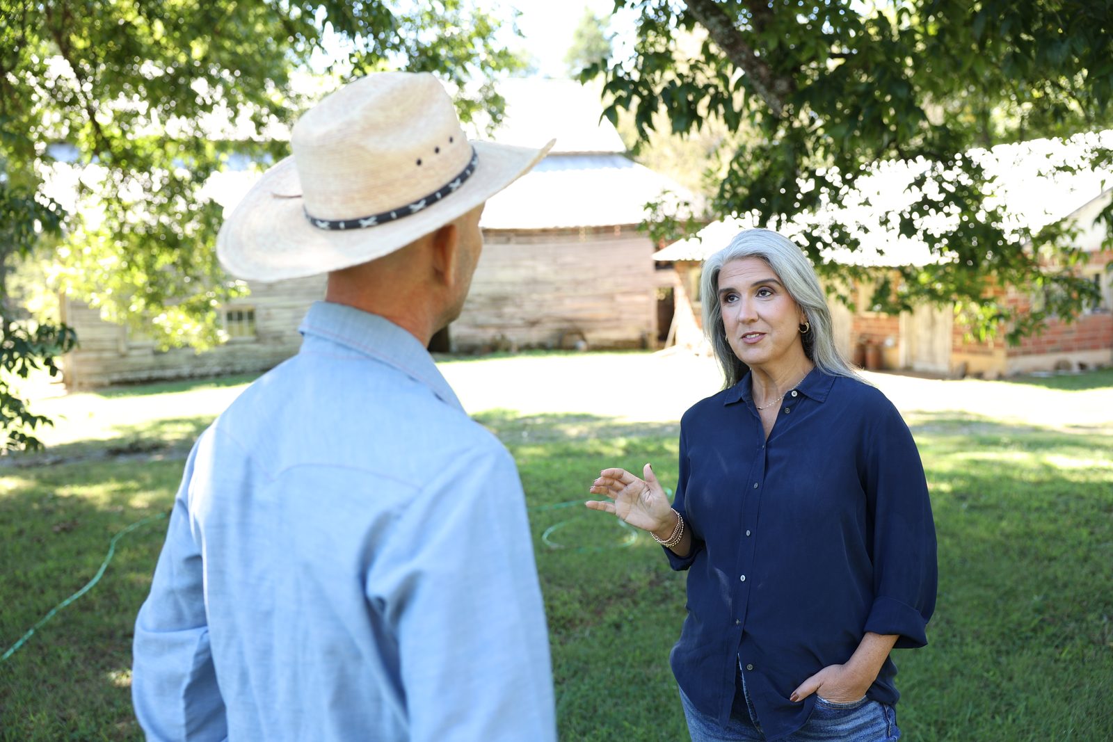 April Montgomery talking with a man in a straw hat outside a farm building.